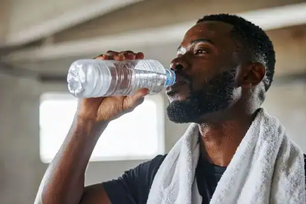 Image of man drinking water to improve hydration Addlestone after work out.